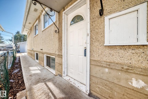 The property features an exterior with a textured finish, a white entry door with an arched window, and a concrete pathway leading alongside the building - 12411 126 Street Nw, Edmonton, AB - Outdoor With Exterior