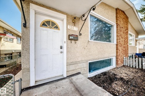 The property features a white front door with an arched window, a brick exterior element, and large windows providing natural light - 12411 126 Street Nw, Edmonton, AB - Outdoor With Exterior