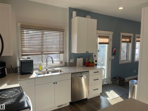 The kitchen features white cabinetry, stainless steel appliances, a double basin sink, and a large window with blinds - 15220 105 Avenue, Edmonton, AB - Indoor Photo Showing Kitchen With Double Sink