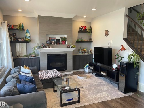 Spacious living area featuring a fireplace with a light-toned surround, built-in shelving and cabinetry, and hardwood style flooring - 15220 105 Avenue, Edmonton, AB - Indoor Photo Showing Living Room With Fireplace