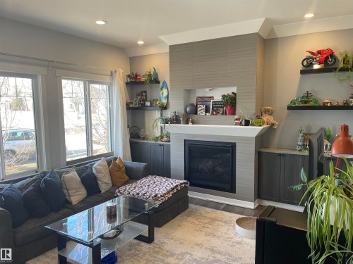Inviting living area featuring large windows, a fireplace with a tiled surround, built-in shelving, and recessed lighting - 15220 105 Avenue, Edmonton, AB - Indoor Photo Showing Living Room With Fireplace