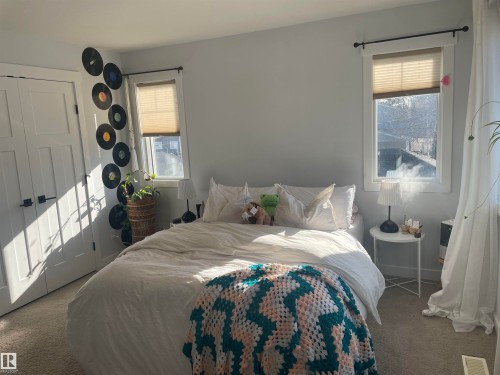 This room features light gray walls, two windows with blinds, and white double doors with black hardware - 15220 105 Avenue, Edmonton, AB - Indoor Photo Showing Bedroom