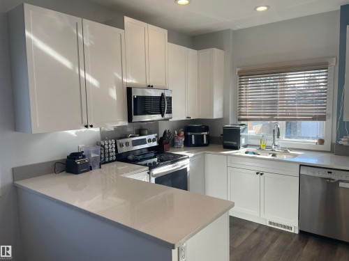 The kitchen features white cabinetry, light-colored countertops, a stainless steel microwave, and a stainless steel dishwasher - 15220 105 Avenue, Edmonton, AB - Indoor Photo Showing Kitchen With Stainless Steel Kitchen With Double Sink