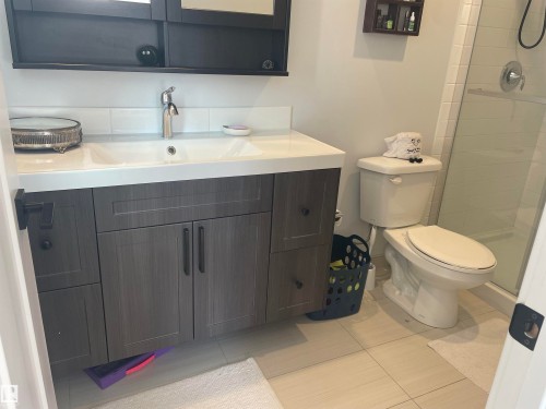 Bathroom featuring a vanity with a white countertop and double sinks, a modern toilet, and a glass-enclosed shower - 15220 105 Avenue, Edmonton, AB - Indoor Photo Showing Bathroom