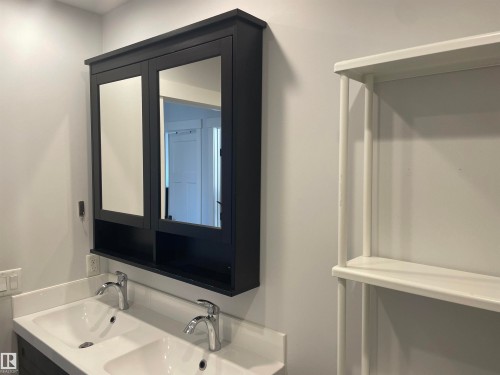 This bathroom features a double vanity with two sinks and chrome fixtures, complemented by a black mirrored medicine cabinet with open shelving - 15220 105 Avenue, Edmonton, AB - Indoor Photo Showing Bathroom