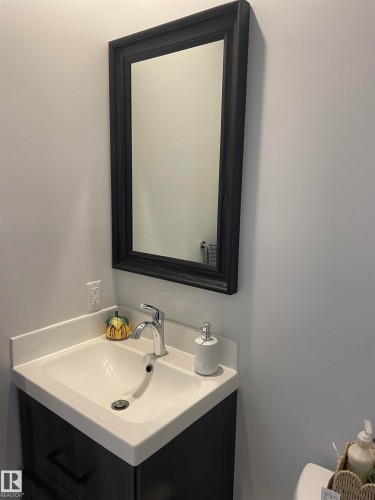 Vanity featuring a white countertop with integrated sink, chrome faucet, and dark wood-look cabinetry - 15220 105 Avenue, Edmonton, AB - Indoor Photo Showing Bathroom