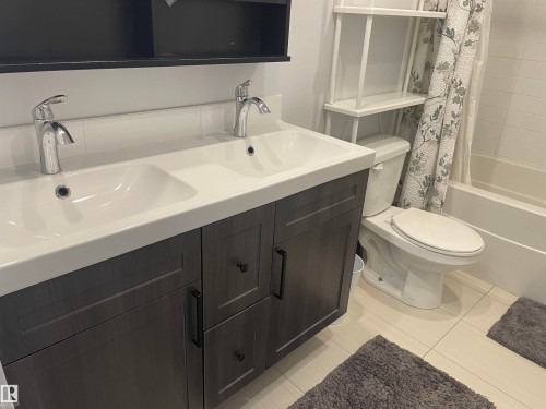 Bathroom featuring a double vanity with two sinks and chrome faucets, a toilet, and a bathtub with a shower curtain - 15220 105 Avenue, Edmonton, AB - Indoor Photo Showing Bathroom
