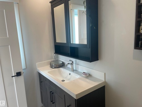 Bathroom vanity with an integrated sink, polished chrome faucet, and a wall-mounted mirrored cabinet - 15220 105 Avenue, Edmonton, AB - Indoor Photo Showing Bathroom