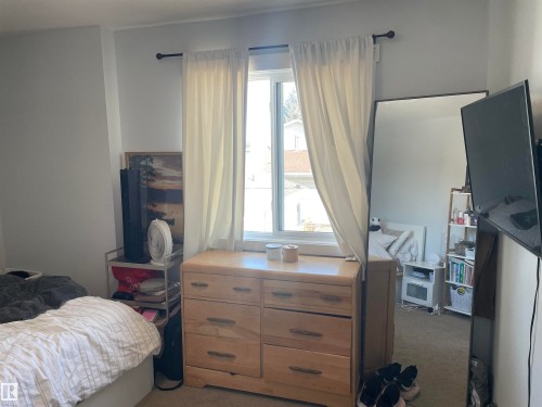 The room features a window with white curtains, natural light, and light-colored walls - 15220 105 Avenue, Edmonton, AB - Indoor Photo Showing Bedroom