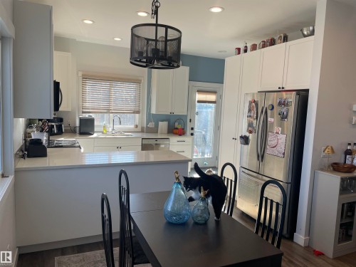 The kitchen features white cabinetry, a stainless steel refrigerator, and recessed lighting - 15220 105 Avenue, Edmonton, AB - Indoor
