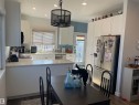 The kitchen features white cabinetry, a stainless steel refrigerator, and recessed lighting - 15220 105 Avenue, Edmonton, AB  - Indoor 