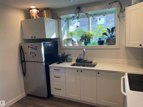 Kitchen featuring white cabinetry, a stainless steel refrigerator, a double basin sink, and a window with a view - 15220 105 Avenue, Edmonton, AB - Indoor Photo Showing Kitchen With Double Sink