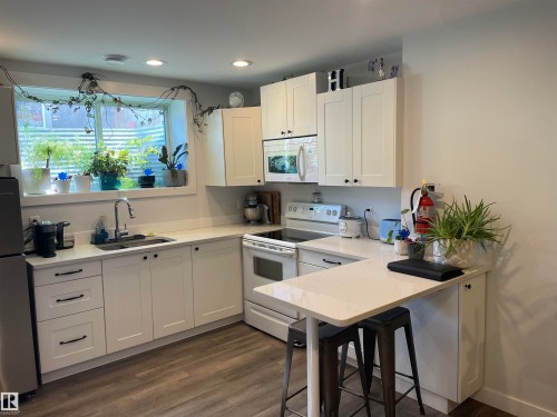 The kitchen features white cabinetry, a built-in microwave, and a stainless steel refrigerator - 15220 105 Avenue, Edmonton, AB - Indoor Photo Showing Kitchen With Double Sink