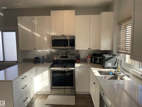The kitchen features white cabinetry, stainless steel appliances, a double basin sink, and ample countertop space - 15220 105 Avenue, Edmonton, AB - Indoor Photo Showing Kitchen With Double Sink