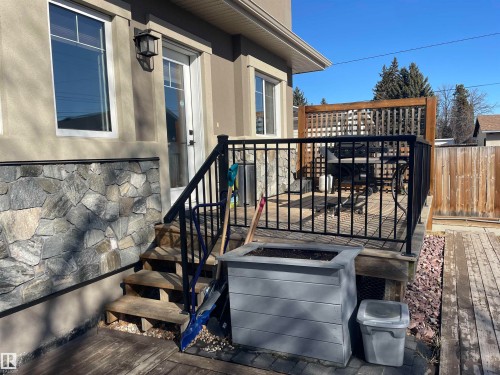 This property features an exterior with stone detailing, a deck with black metal railings, and a wooden fence - 15220 105 Avenue, Edmonton, AB - Outdoor With Deck Patio Veranda With Exterior