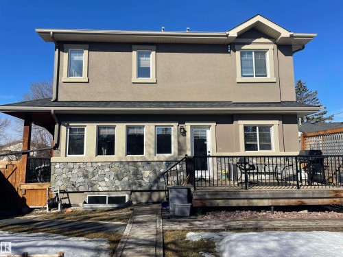 The property features a two-story exterior with a stucco finish and stone accents on the lower level - 15220 105 Avenue, Edmonton, AB - Outdoor With Deck Patio Veranda