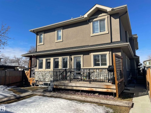 The property features a private wooden deck with black metal railings, a stone-accented exterior, and a wooden privacy screen - 15220 105 Avenue, Edmonton, AB - Outdoor With Deck Patio Veranda