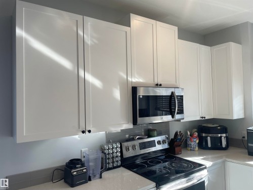 Kitchen featuring white upper cabinetry, a stainless steel microwave, and a stainless steel electric range - 15220 105 Avenue, Edmonton, AB - Indoor Photo Showing Kitchen