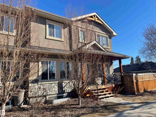 The property features a stucco exterior with stone accents on the lower level, a covered front porch with wooden support beams, and an exterior wooden fence - 15220 105 Avenue, Edmonton, AB - Outdoor