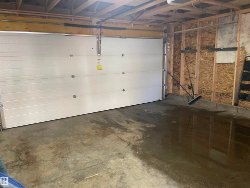Garage interior with a large white sectional garage door and exposed wooden framing - 15220 105 Avenue, Edmonton, AB - Indoor Photo Showing Garage