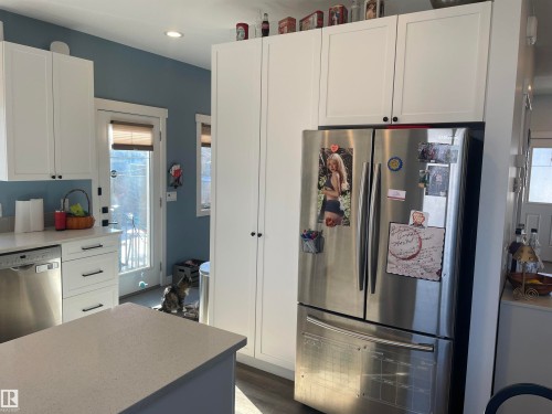The kitchen features white cabinetry with black hardware, stainless steel appliances, a light-colored countertop, and a kitchen island - 15220 105 Avenue, Edmonton, AB - Indoor Photo Showing Kitchen With Stainless Steel Kitchen