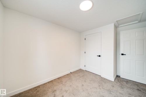This room features white walls, carpet flooring, a circular ceiling light fixture, and two white doors with dark hardware - 125 Woodborough Way, Edmonton, AB - Indoor Photo Showing Other Room