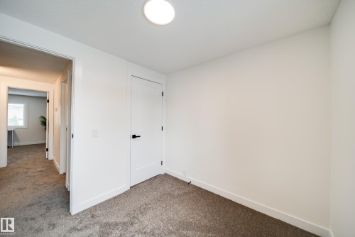 This room features plush carpet flooring, white walls, and a modern white door with a black handle - 125 Woodborough Way, Edmonton, AB - Indoor Photo Showing Other Room
