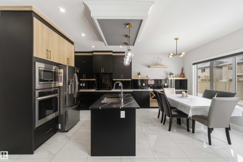 The kitchen features dark cabinetry with light wood accents, stainless steel appliances, and a central island with a sink and a light-colored countertop - 1520 151 Avenue, Edmonton, AB - Indoor