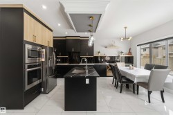 The kitchen features dark cabinetry with light wood accents, stainless steel appliances, and a central island with a sink and a light-colored countertop - 