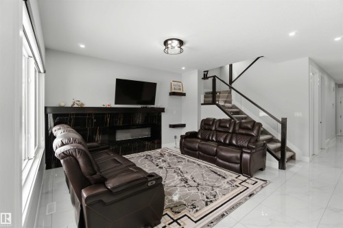 The living area features a modern fireplace with a black marble-style surround, large windows, and sleek tile flooring - 1520 151 Avenue, Edmonton, AB - Indoor