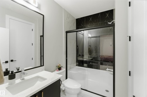 Bathroom featuring a white vanity with a rectangular sink, a black framed mirror, and a shower with black marble-look tiling and a clear glass enclosure - 1520 151 Avenue, Edmonton, AB - Indoor Photo Showing Bathroom