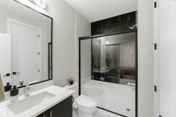 Bathroom featuring a white vanity with a rectangular sink, a black framed mirror, and a shower with black marble-look tiling and a clear glass enclosure - 