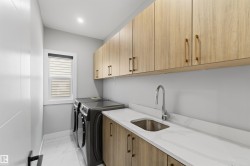 Well-appointed laundry area featuring light wood cabinetry with gold hardware, a white countertop with an integrated sink, and white tiled flooring - 