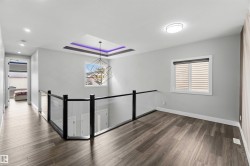 This upstairs landing features wood-look flooring, a modern geometric chandelier with purple accent lighting, and a glass and black railing - 