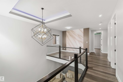 The property features an open landing with wood flooring, glass railings, and a contemporary chandelier - 1520 151 Avenue, Edmonton, AB - Indoor Photo Showing Other Room