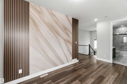Contemporary interior space featuring wide plank flooring, a wall with marble-patterned detailing, and slat wood accent panels - 