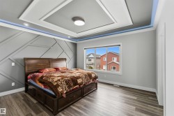 This bedroom features tray ceilings with integrated lighting, a decorative accent wall, and a window providing views of the neighborhood - 