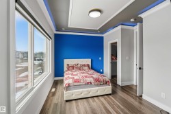 Spacious room featuring large windows, wood-look flooring, a tray ceiling with accent lighting, and a brightly painted accent wall - 