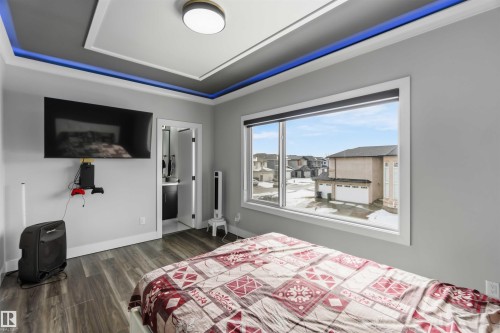The room features a tray ceiling with accent lighting, rich wood-look flooring, and a large window providing ample natural light and views of the surrounding neighborhood - 1520 151 Avenue, Edmonton, AB - Indoor Photo Showing Bedroom