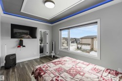 The room features a tray ceiling with accent lighting, rich wood-look flooring, and a large window providing ample natural light and views of the surrounding neighborhood - 