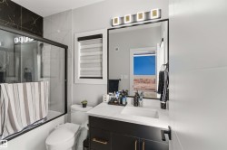 Bathroom featuring a vanity with a white countertop and dark cabinetry, a framed mirror with overhead lighting, and a glass-enclosed shower with contrasting wall tiles - 