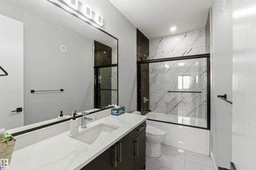 Contemporary bathroom featuring a vanity with a white countertop, a large mirror with integrated lighting, and a bathtub with a sliding glass door and tiled surround - 1520 151 Avenue, Edmonton, AB - Indoor Photo Showing Bathroom