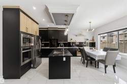 The kitchen features dark cabinetry, light wood upper cabinets, stainless steel appliances, and a central island with a sink - 
