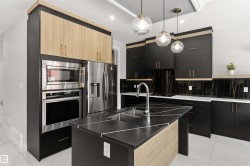 This kitchen features a central island with a sink and a black countertop with white veining - 