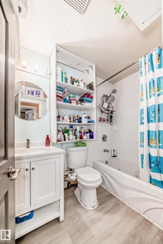 The bathroom features a vanity with a white cabinet and a white countertop, a toilet, and a bathtub with a shower and a shower curtain - 16305 107A Ave, Edmonton, AB - Indoor Photo Showing Bathroom