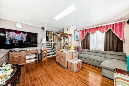 Living area featuring hardwood floors, a staircase with a white railing, and a window with curtains - 16305 107A Ave, Edmonton, AB - Indoor Photo Showing Living Room
