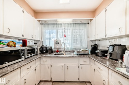The kitchen features white cabinetry, a double sink with a gooseneck faucet, and ample counter space with a patterned countertop - 16305 107A Ave, Edmonton, AB - Indoor Photo Showing Kitchen