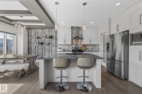 The kitchen features white cabinetry, stainless steel appliances, a mosaic tile backsplash, and a central island with bar seating - 3864 Robins Crescent, Edmonton, AB - Indoor Photo Showing Kitchen With Upgraded Kitchen