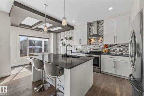 The kitchen features a spacious island with a dark countertop, white cabinetry, a stylish tiled backsplash, and stainless steel appliances - 3864 Robins Crescent, Edmonton, AB - Indoor Photo Showing Kitchen With Upgraded Kitchen