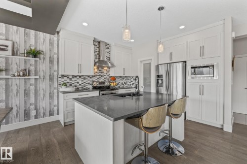 The kitchen features white cabinetry, stainless steel appliances, a mosaic tile backsplash, and a central island with a dark countertop and pendant lighting - 3864 Robins Crescent, Edmonton, AB - Indoor Photo Showing Kitchen With Double Sink With Upgraded Kitchen